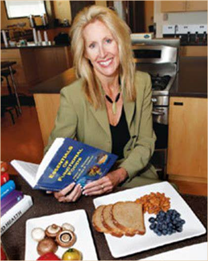 Dr. Clare Hasler early in her nutrition career pictured with a book and plates of healthy food in front of her